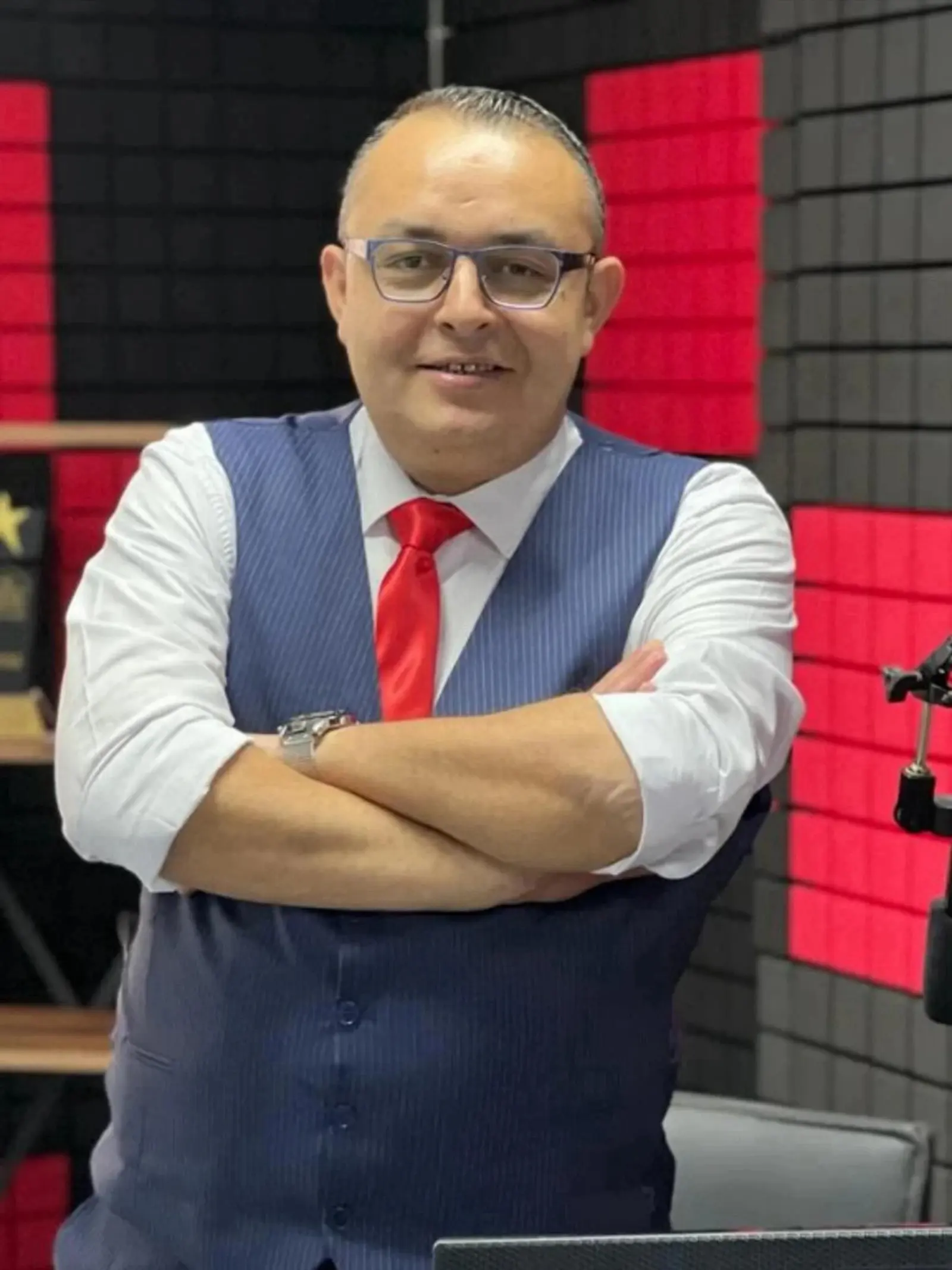 Dadali, radyo stüdyosunda kırmızı akustik panellerin önünde kollarını kavuşturmuş duruyor.